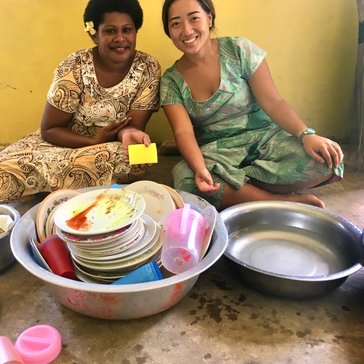 Asian Pacific American Volunteer sits with Fijian woman washing dishes