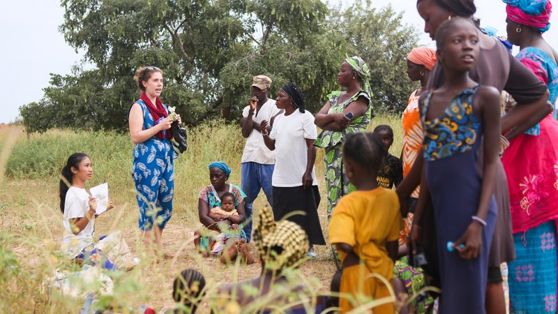 A American female volunteer stands in a field with many Senegalese individuals.