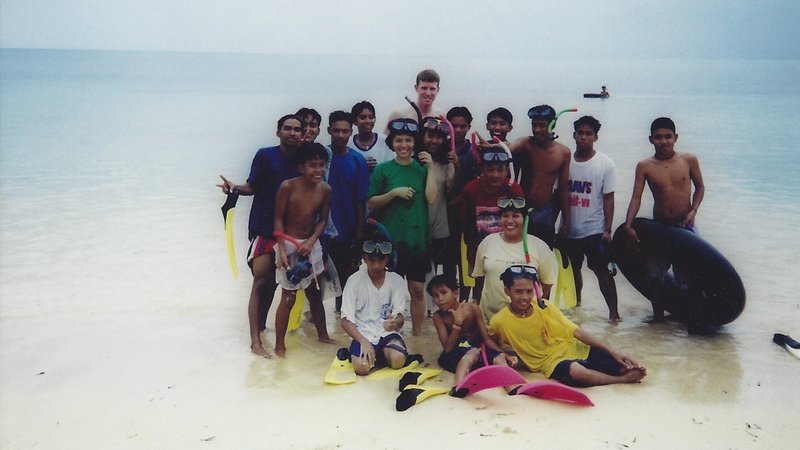 An American male stands with teenage Filipino students in clear blue waters.