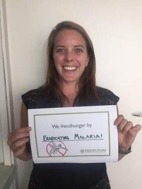 A female Volunteer holds a sign saying she will fight food insecurity by fighting malaria